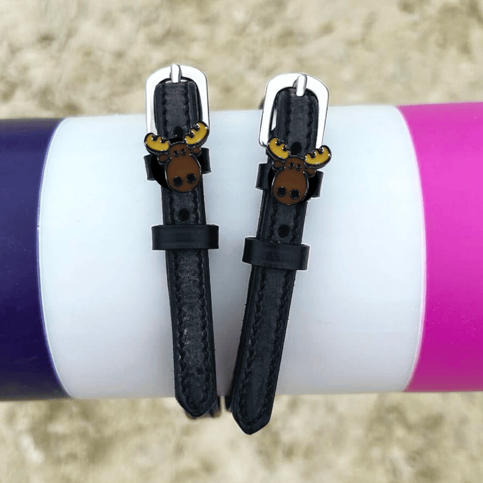 ManeJane moose spur straps draped over a colorful jump pole in a sand arena