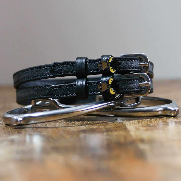 Black moose head spur straps stacked on a silver spur on wood, close-up
