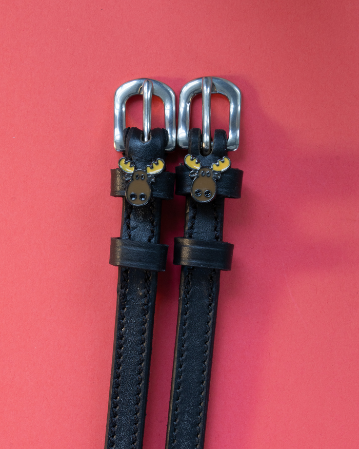 Pair of black leather moose head spur straps flat-laid on a coral background