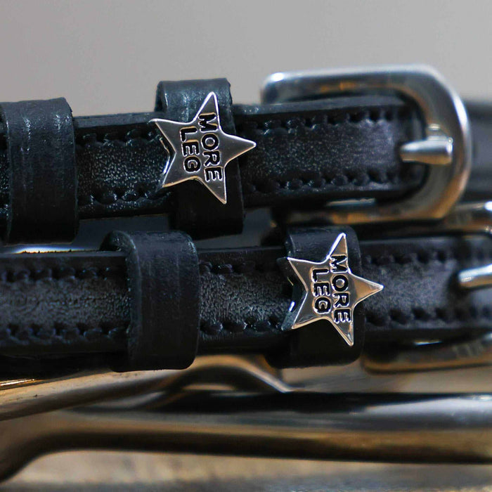 Close-up of silver MORE LEG star charms on black leather spur strap keepers