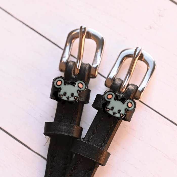 Close-up of grey mouse charms on black spur straps with silver buckles on pink planks