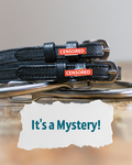 ManeJane Mystery spur straps with red CENSORED charms beside an It's a Mystery text card