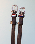 Brown leather ManeJane spur straps with silver buckles and Netherlands flag charms on grey