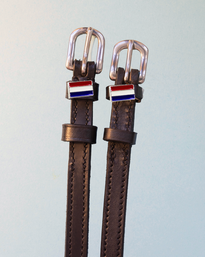 Brown leather ManeJane spur straps with silver buckles and Netherlands flag charms on grey