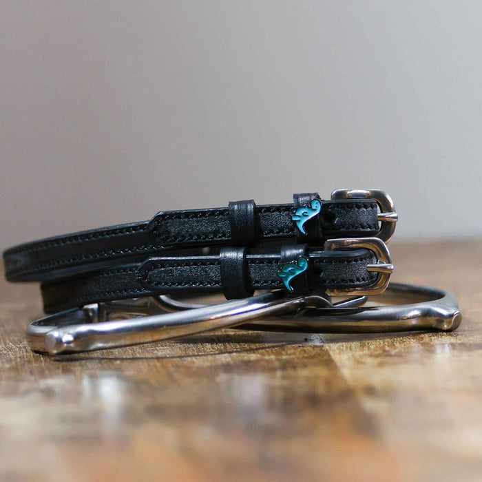 Nice Dino spur straps coiled beside a stirrup on a wooden tabletop