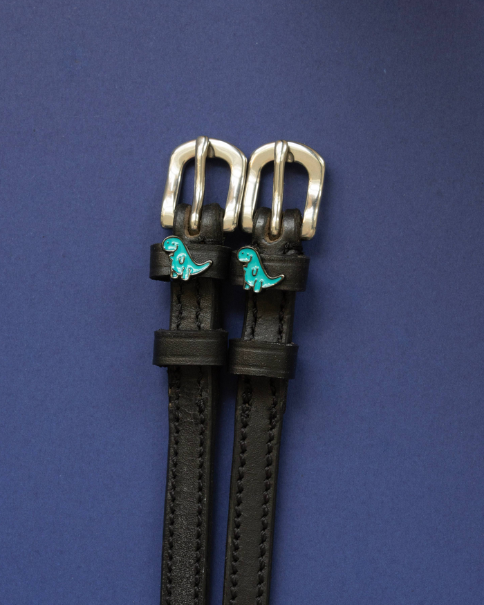 Black leather dinosaur charm spur straps flat-laid on a deep navy background