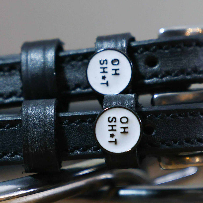 Close-up of round OH SH*T text charms on black leather spur strap keepers