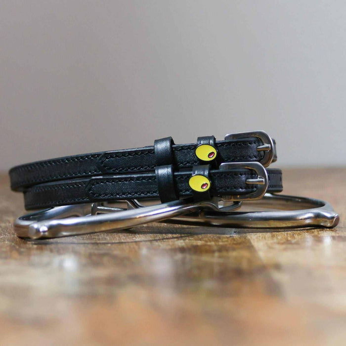 Black leather olive spur straps coiled on a wooden surface with a silver bit