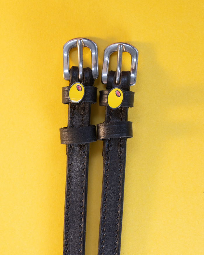 Dark leather spur straps with yellow-green olive charms flat-laid on a yellow background
