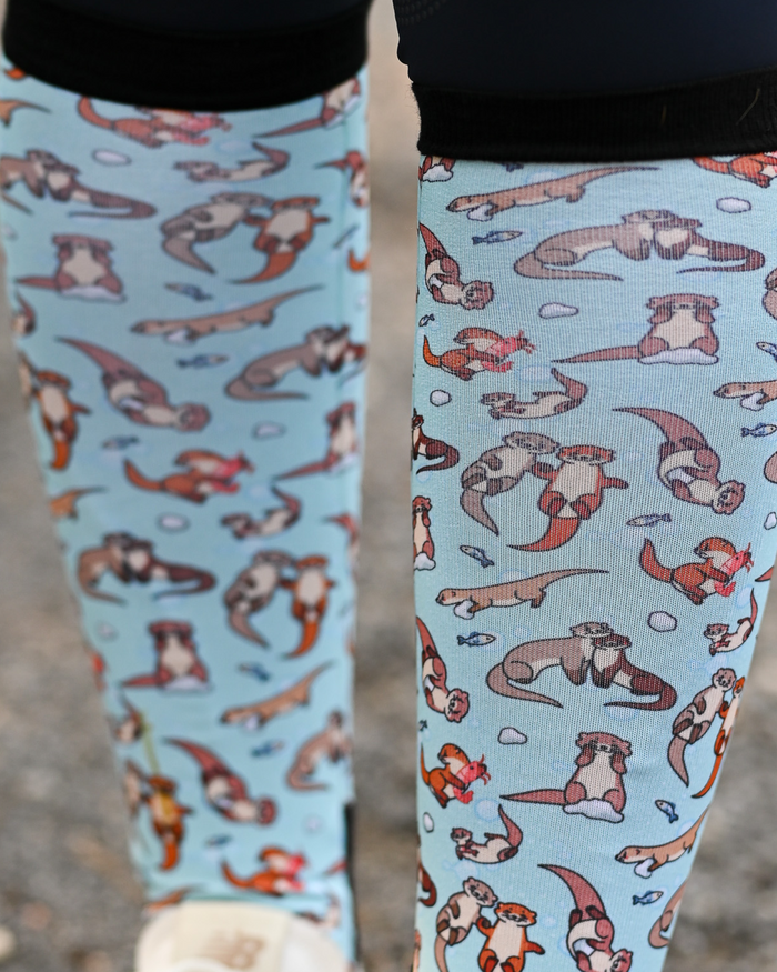 Close crop of the Otter-ly Adorable boot sock print, otters floating and holding hands on pale blue