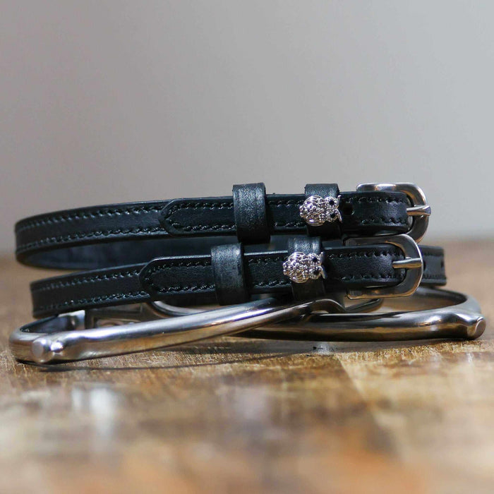 Black leather owl bling spur straps coiled beside a silver spur on a wood surface