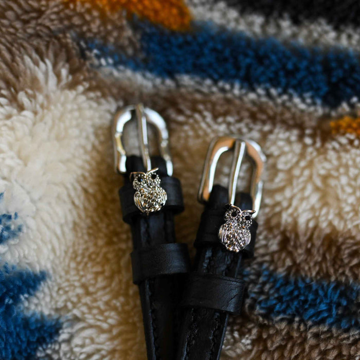 Black leather crystal owl spur straps with silver buckles laid on a cozy sherpa blanket