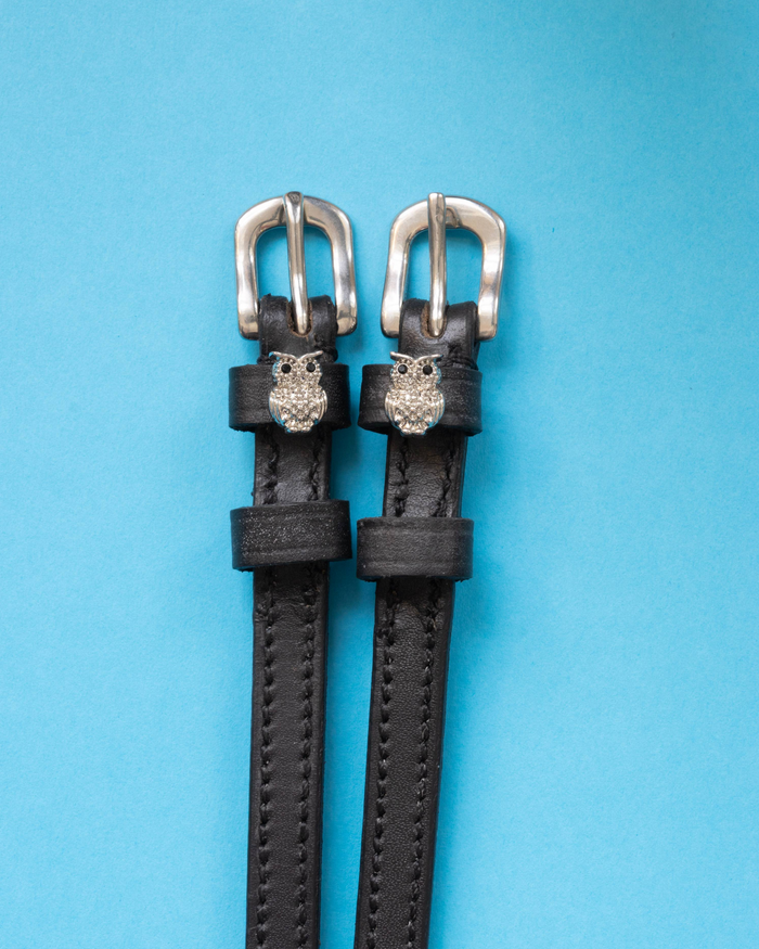 Pair of black leather owl bling spur straps with silver buckles on a light blue background