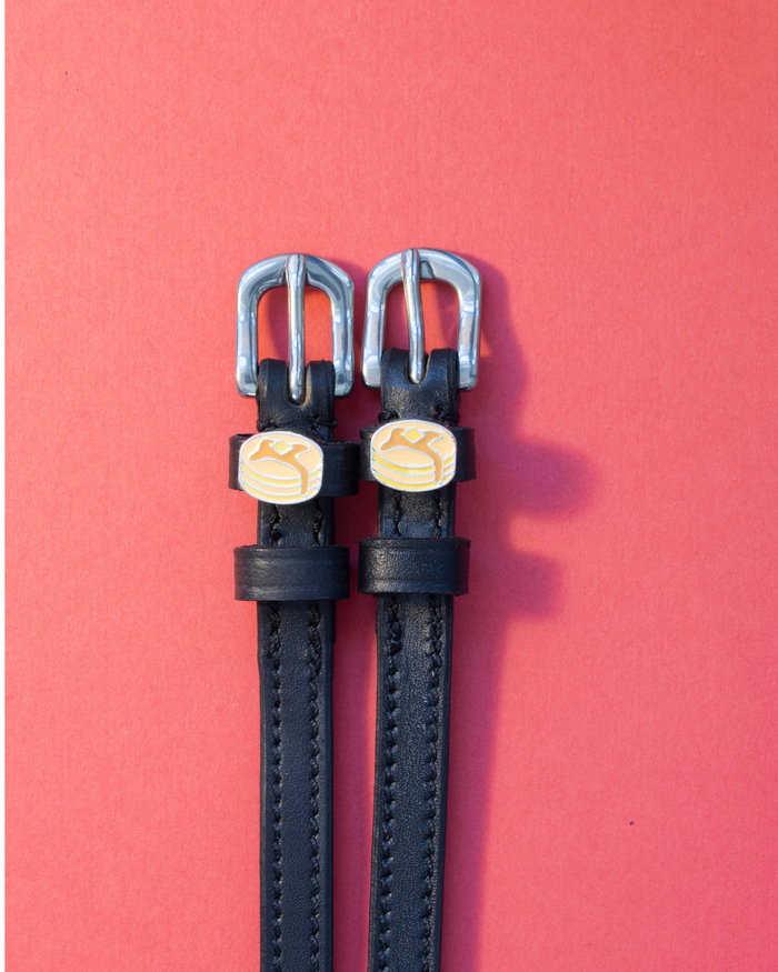 Pair of black leather pancake spur straps laid flat on a coral background