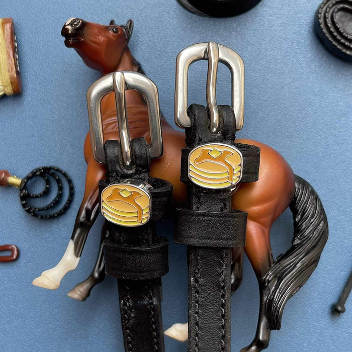 ManeJane pancake spur straps staged with a toy horse on a blue background