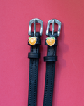 Pair of black leather ManeJane spur straps with silver buckles and glittery peach charms on pink