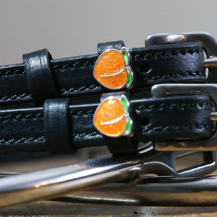Close-up of a sparkly orange peach charm on a black leather spur strap keeper