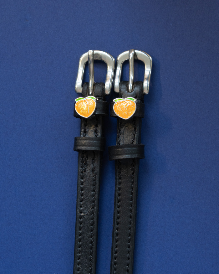 Black leather peach spur straps flat-laid on a deep blue background
