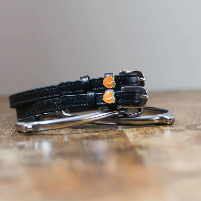 Black leather peach spur straps coiled beside a silver spur on wood