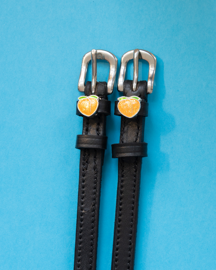 Pair of black leather peach charm spur straps on a light blue background