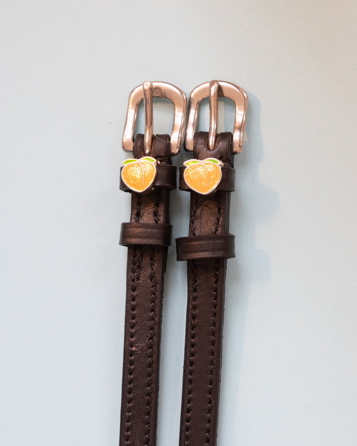 Dark brown leather ManeJane peach spur straps with rose-gold buckles on grey