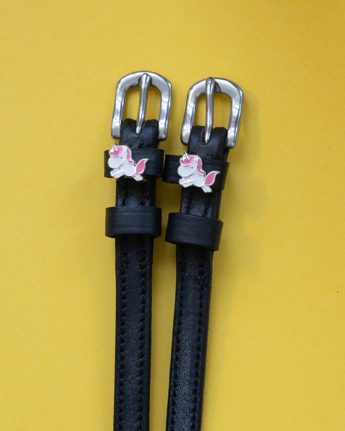 Black leather ManeJane spur straps with silver buckles and chubby unicorn charms on yellow