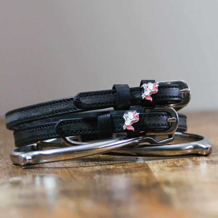 Phat unicorn spur straps coiled on a silver stirrup on a wooden table