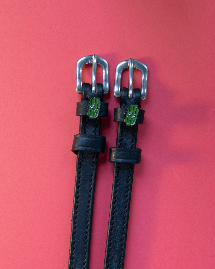 Black leather ManeJane spur straps with silver buckles and green pickle charms on coral red