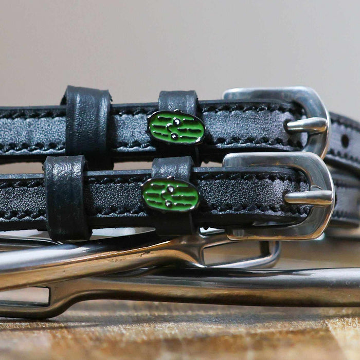 Close-up of smiling green pickle enamel charms on black leather spur strap keepers