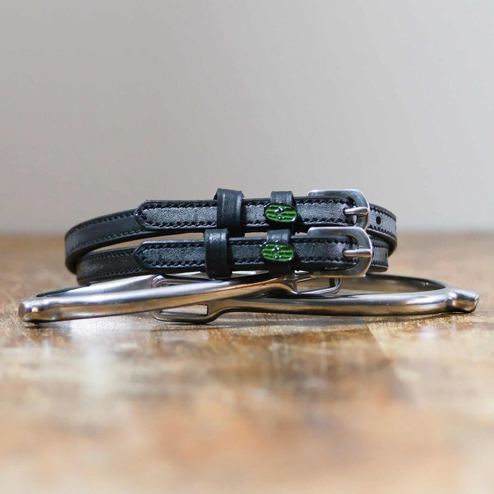 Black leather pickle spur straps coiled beside a silver spur on a wooden surface
