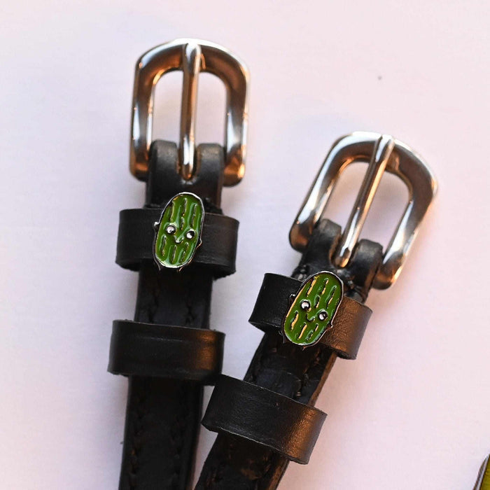 Close-up of two smiling pickle charms on black leather ManeJane spur straps over pink