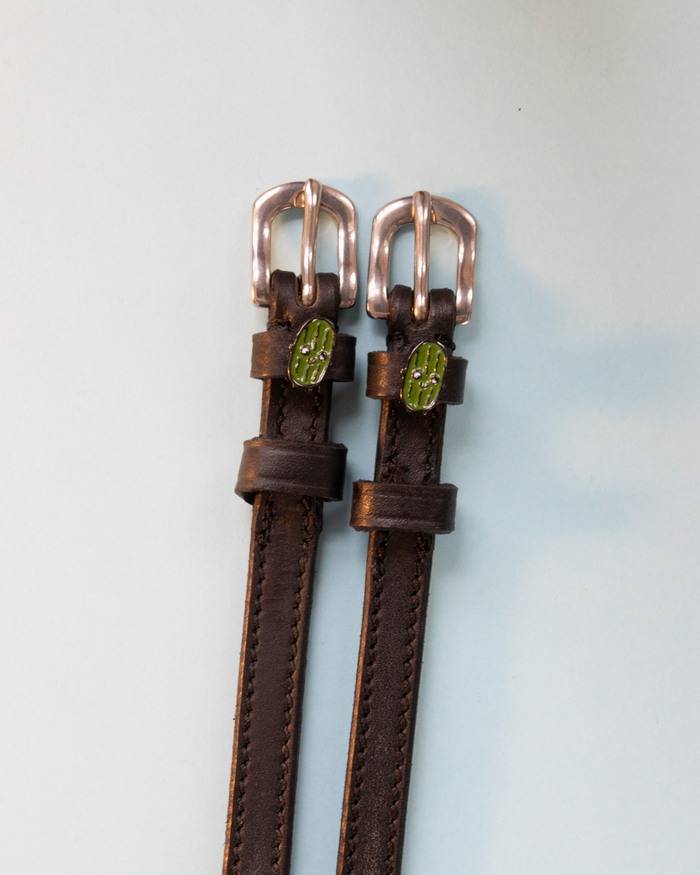 Brown leather pickle spur straps with rose gold buckles on a pale blue background