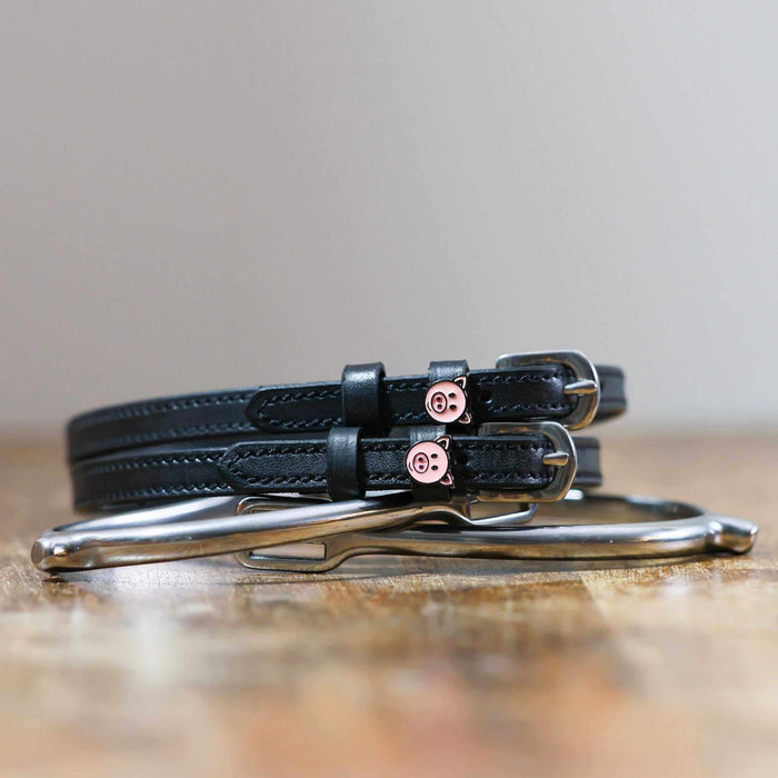 Coiled black leather spur straps and a silver spur on wood with pig-face charms