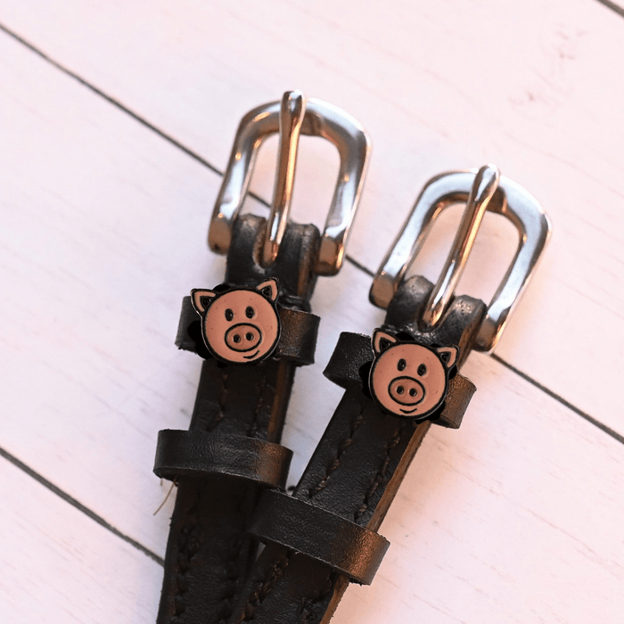 Close-up of pink pig-face charms and silver buckles on black spur straps, pink planks