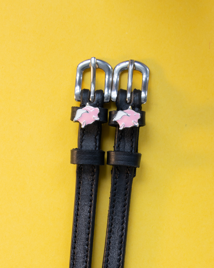 Black leather ManeJane flying pig spur straps with silver buckles on a yellow backdrop