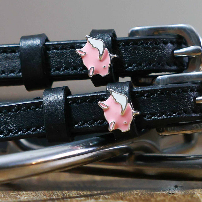 Close-up of pink winged pig charms on black leather spur strap keepers by a stirrup