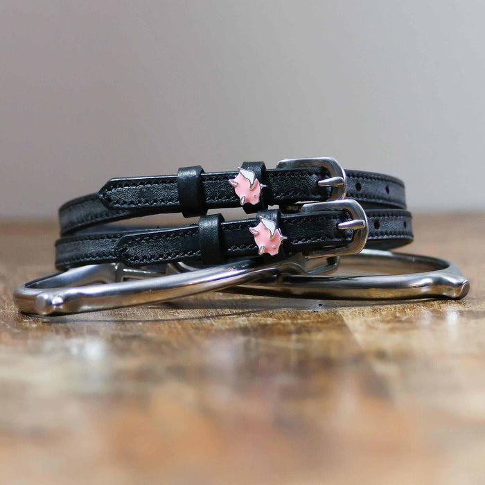 Black leather flying pig spur straps coiled beside a stirrup on wood