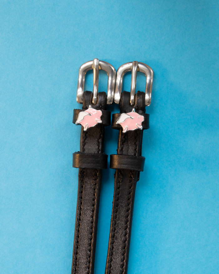 Black leather winged pig charm spur straps on a bright blue background