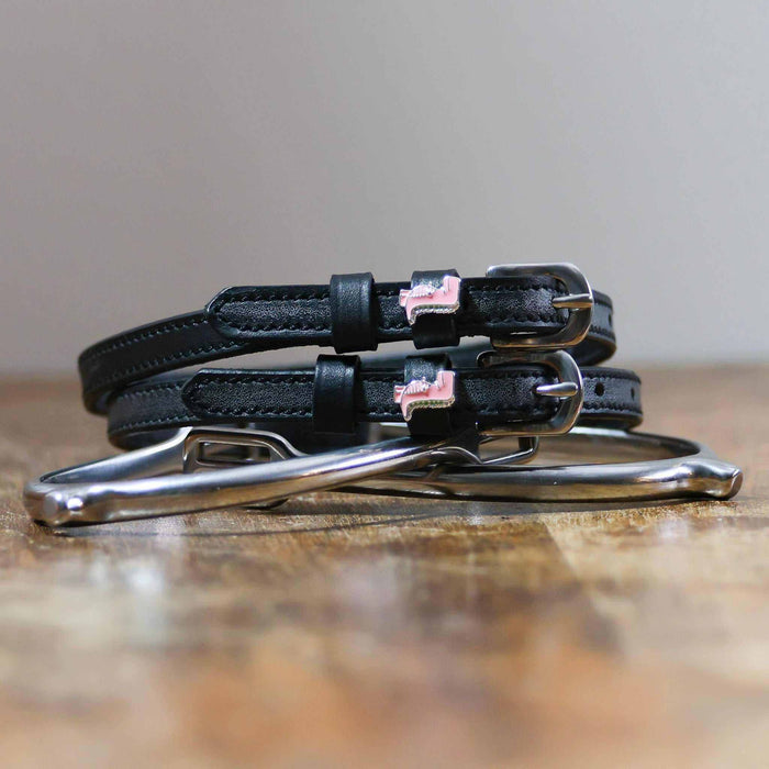 Pink dinosaur spur straps coiled on a silver stirrup on a wooden table