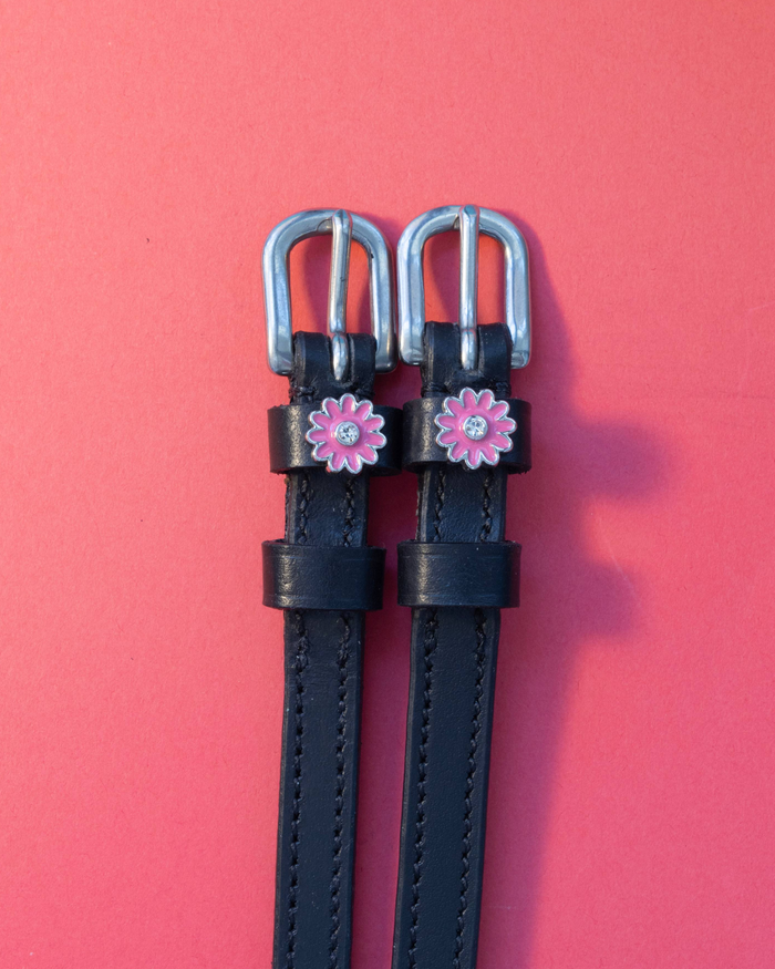 Pair of pink flower spur straps with silver buckles laid flat on a coral background