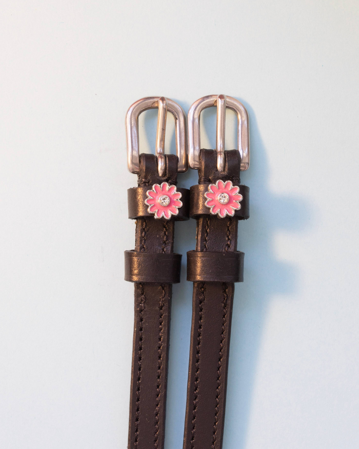 Brown leather ManeJane pink flower spur straps on a soft blue-grey background