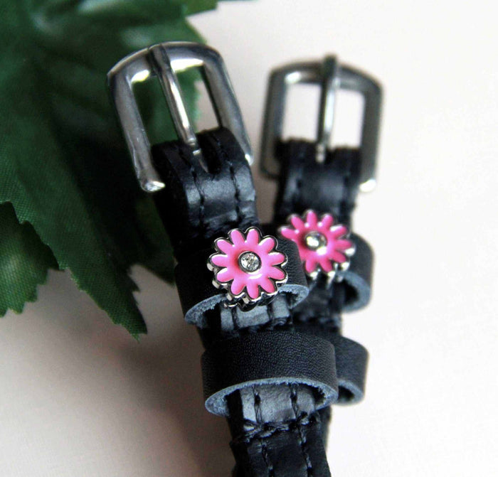 Angled view of pink daisy charm spur straps set against green leaves