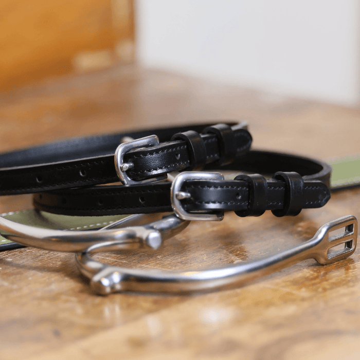 Plain black leather PlainJane spur straps coiled beside a stirrup and green strap