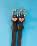 Black leather ManeJane spur straps with pink Pony Love heart charms on a blue background