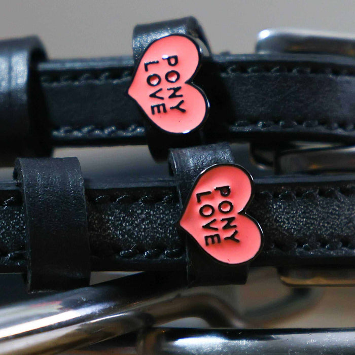 Close-up of pink Pony Love heart charms on black leather ManeJane spur strap keepers