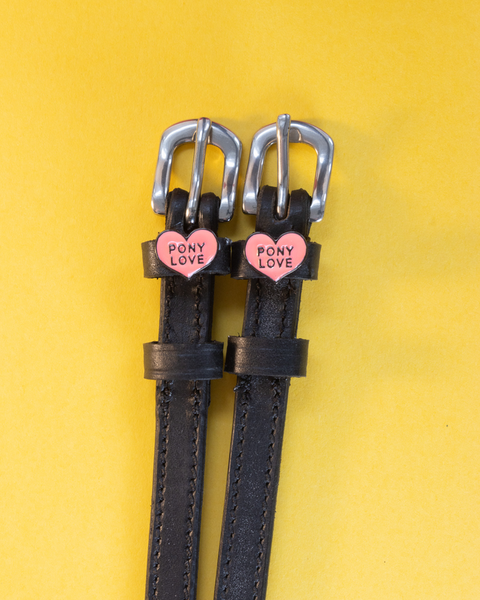 Black leather Pony Love spur straps with silver buckles on a yellow background