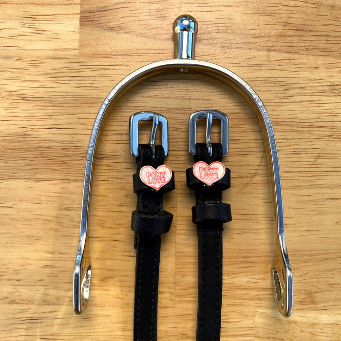 Pony Love spur straps hung from a silver spur bracket on a wood surface