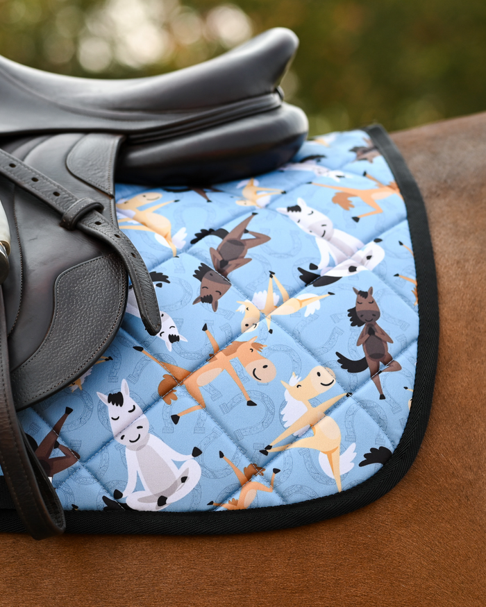 Pony Pilates pad in denim blue with black binding, shown under a black dressage saddle on a bay horse