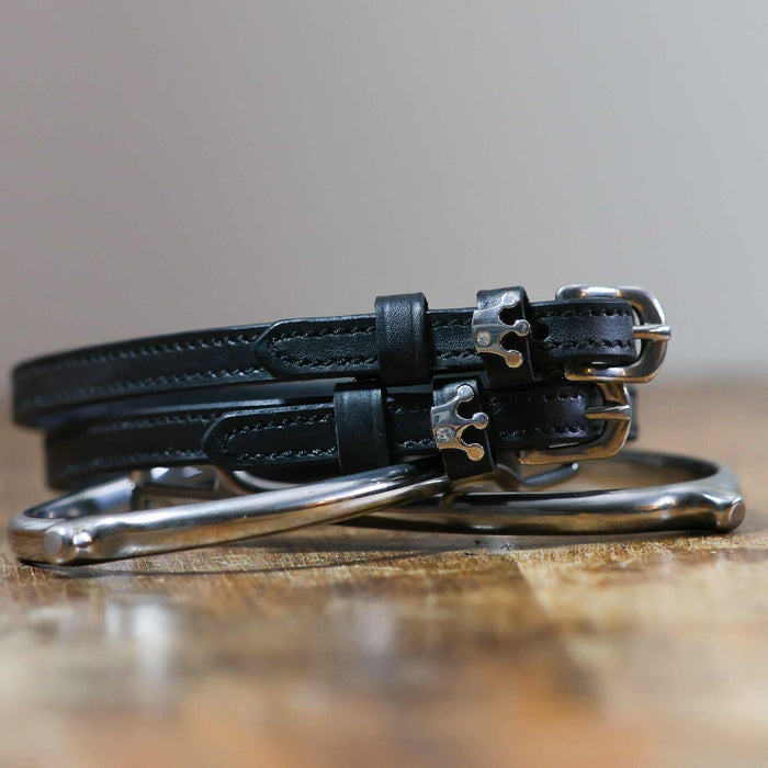 Queenie crown-charm spur straps coiled beside a stirrup on a wooden tabletop