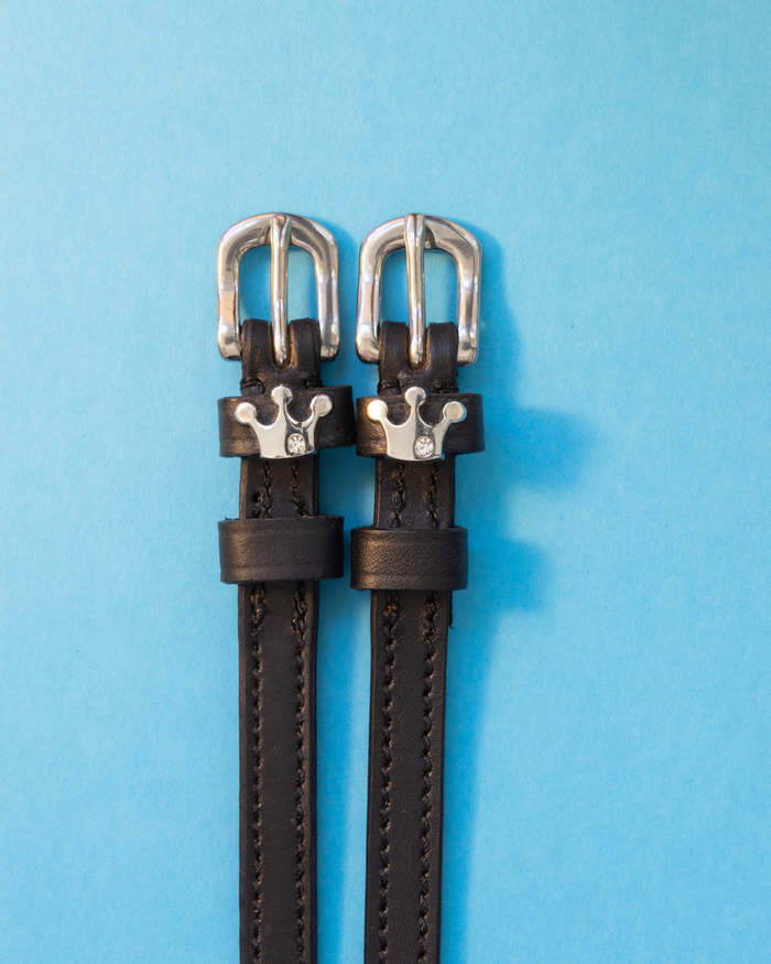 Pair of Queenie crown spur straps with silver buckles laid flat on a blue background